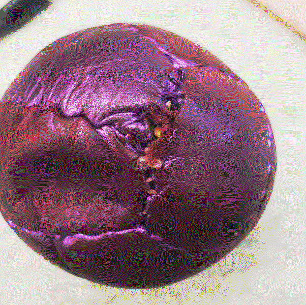 Picture of a purple juggling ball showing a wide open seam with seeds inside